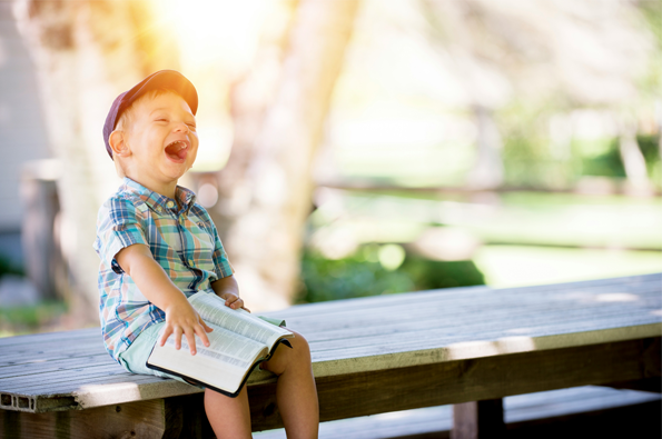 Joyful young lad sitting on an outside bench reading the Bible